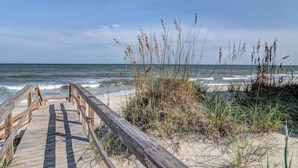 Una pasarela de madera que lleva a una playa con arena y césped.