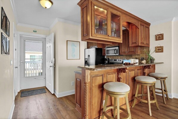 A kitchen with wooden cabinets, a central island with stools, a refrigerator, a microwave, and a sink.
