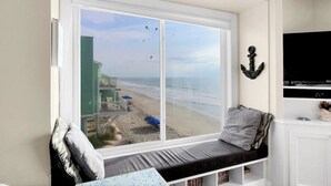 Una habitación con un amplio ventanal con vistas a la playa, un banco acolchado y un televisor montado.
