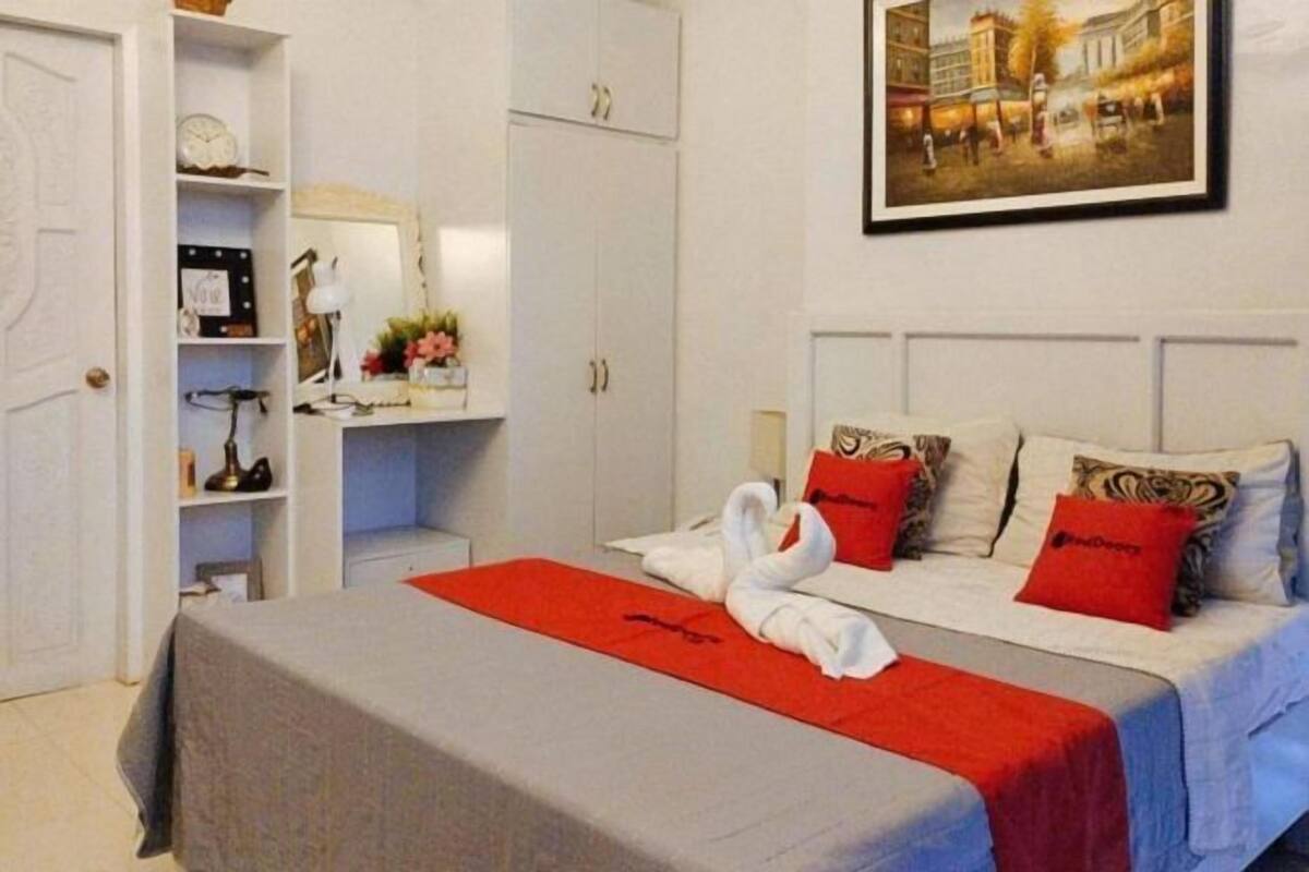 A hotel room with a neatly made bed, a red throw, and a painting on the wall.