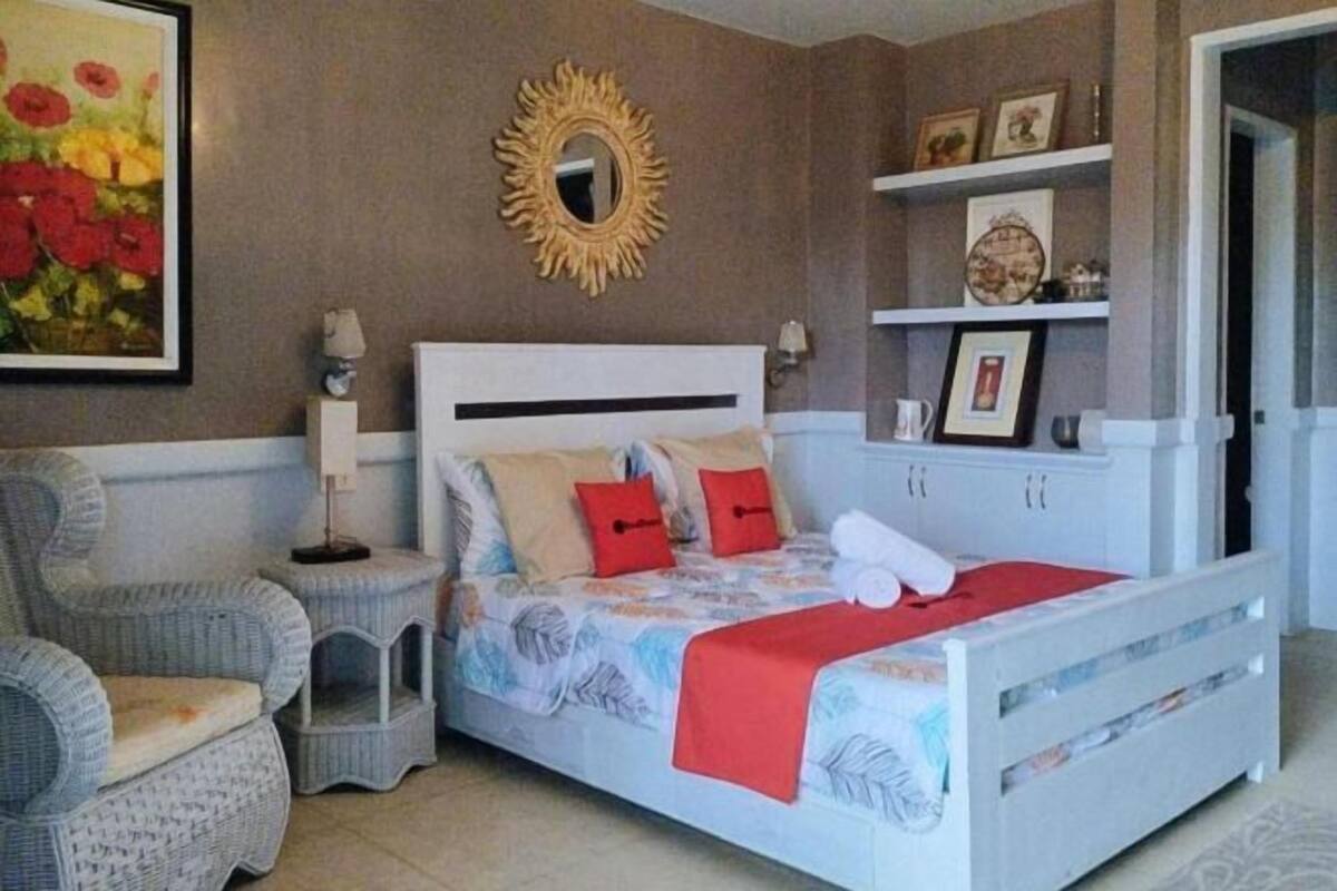 A bedroom with a bed, a chair, a nightstand, a mirror, and shelves with framed pictures.
