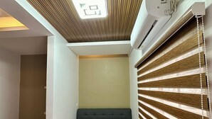 Een kamer met een visgraat parketvloer, een grijze bank, een plafond met een inbouwverlichtingsarmatuur en een wandairconditioning.