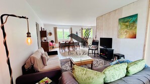A modern living room with a sofa, a coffee table, a TV, and a dining area in the background. - Chavid 17 - Spacieuse Maison Avec Jardin (Échillais)