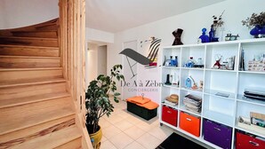 A modern interior with a wooden staircase, a white wall with a logo, and a white shelving unit with various items. - Chavid 17 - Spacieuse Maison Avec Jardin (Échillais)