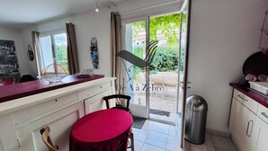 A compact kitchen with a dining area, a window with curtains, and a view of greenery outside. - Chavid 17 - Spacieuse Maison Avec Jardin (Échillais)