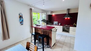 A modern kitchen with a central island, bar stools, and a dining area with a table and chairs. - Chavid 17 - Spacieuse Maison Avec Jardin (Échillais)