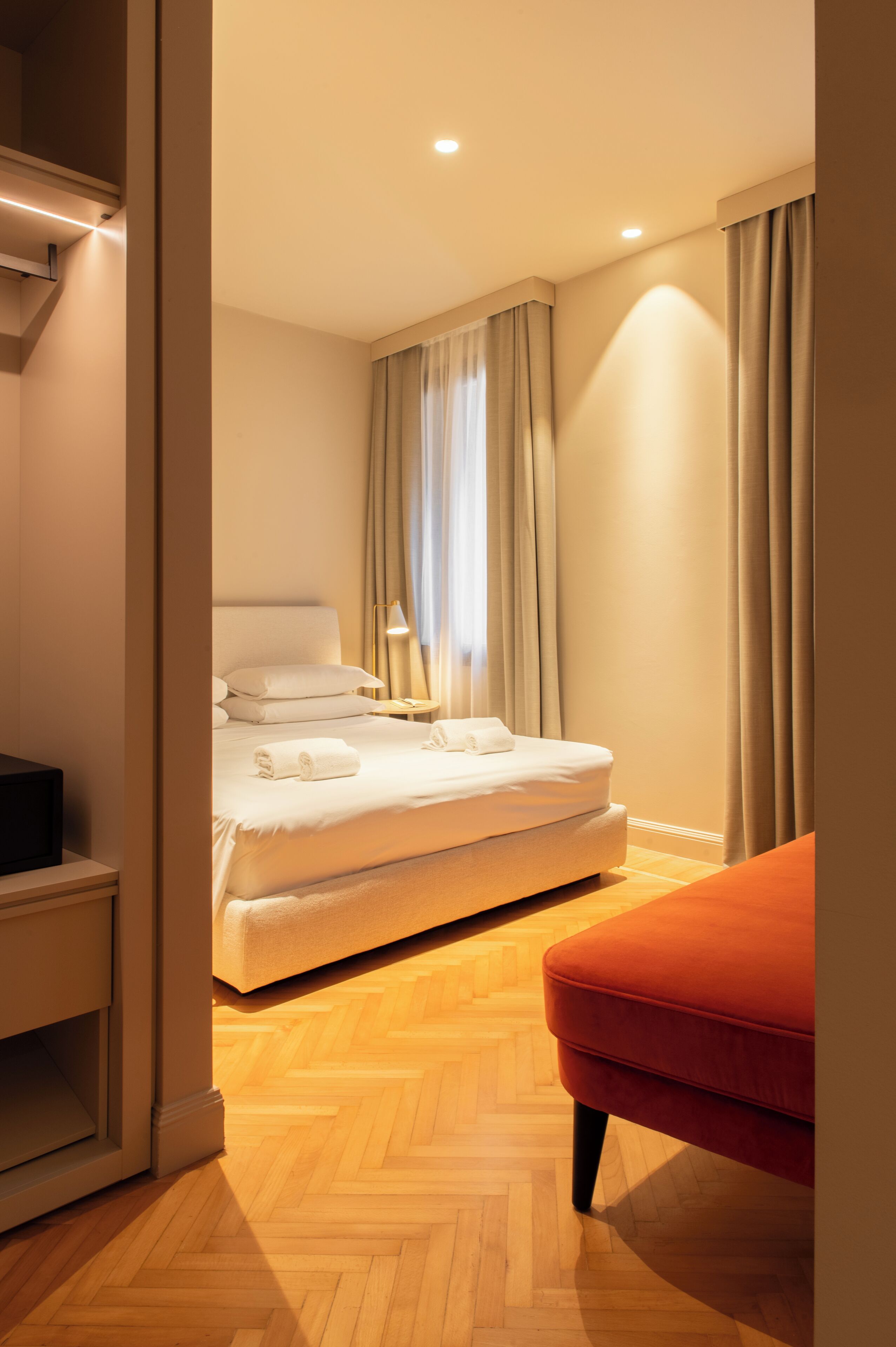 A bedroom with a bed, a nightstand, a red chair, and a wooden floor.