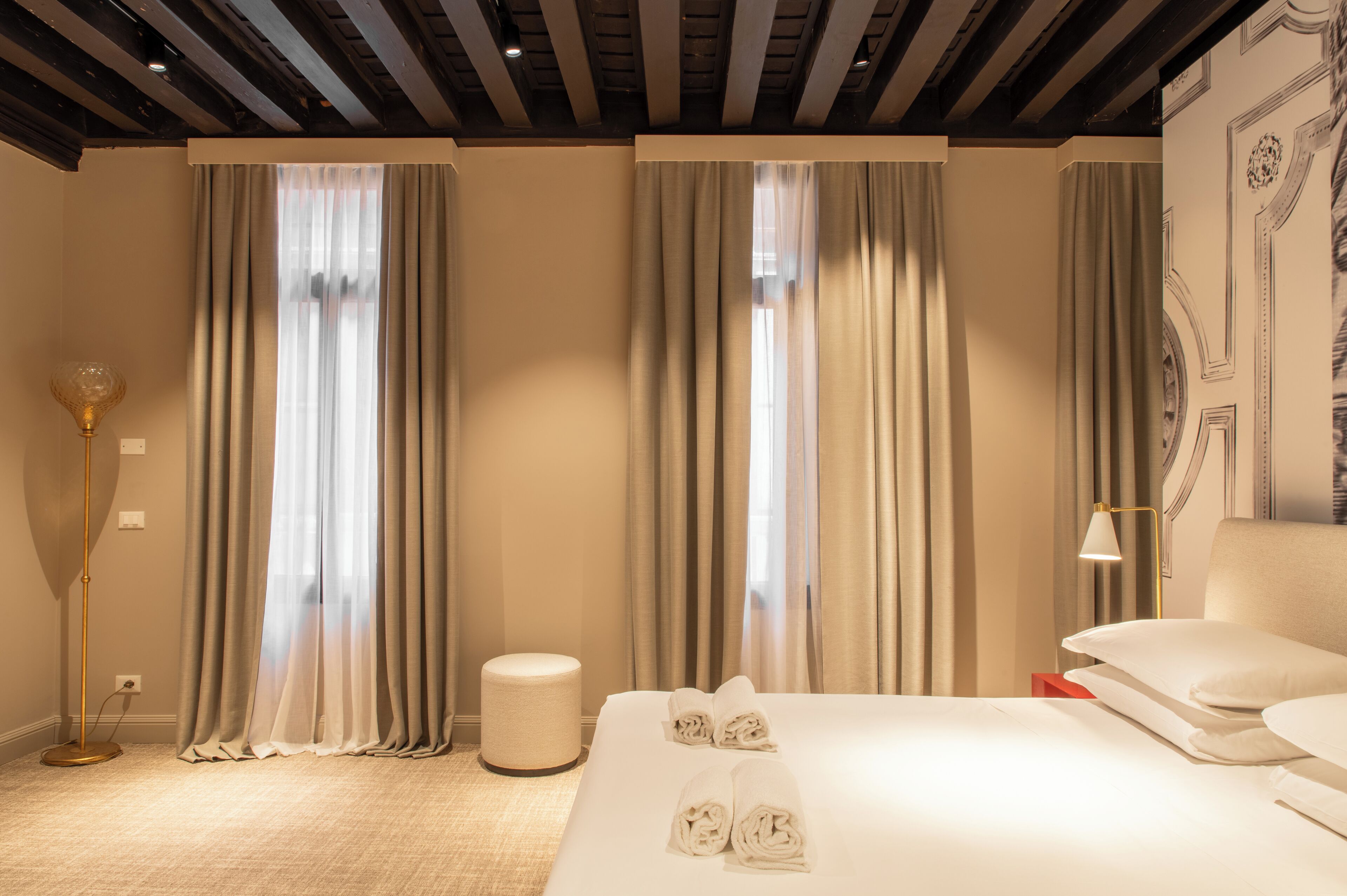 Una habitación de hotel con una cama, cortinas, una lámpara de pie y una pared con un diseño decorativo.