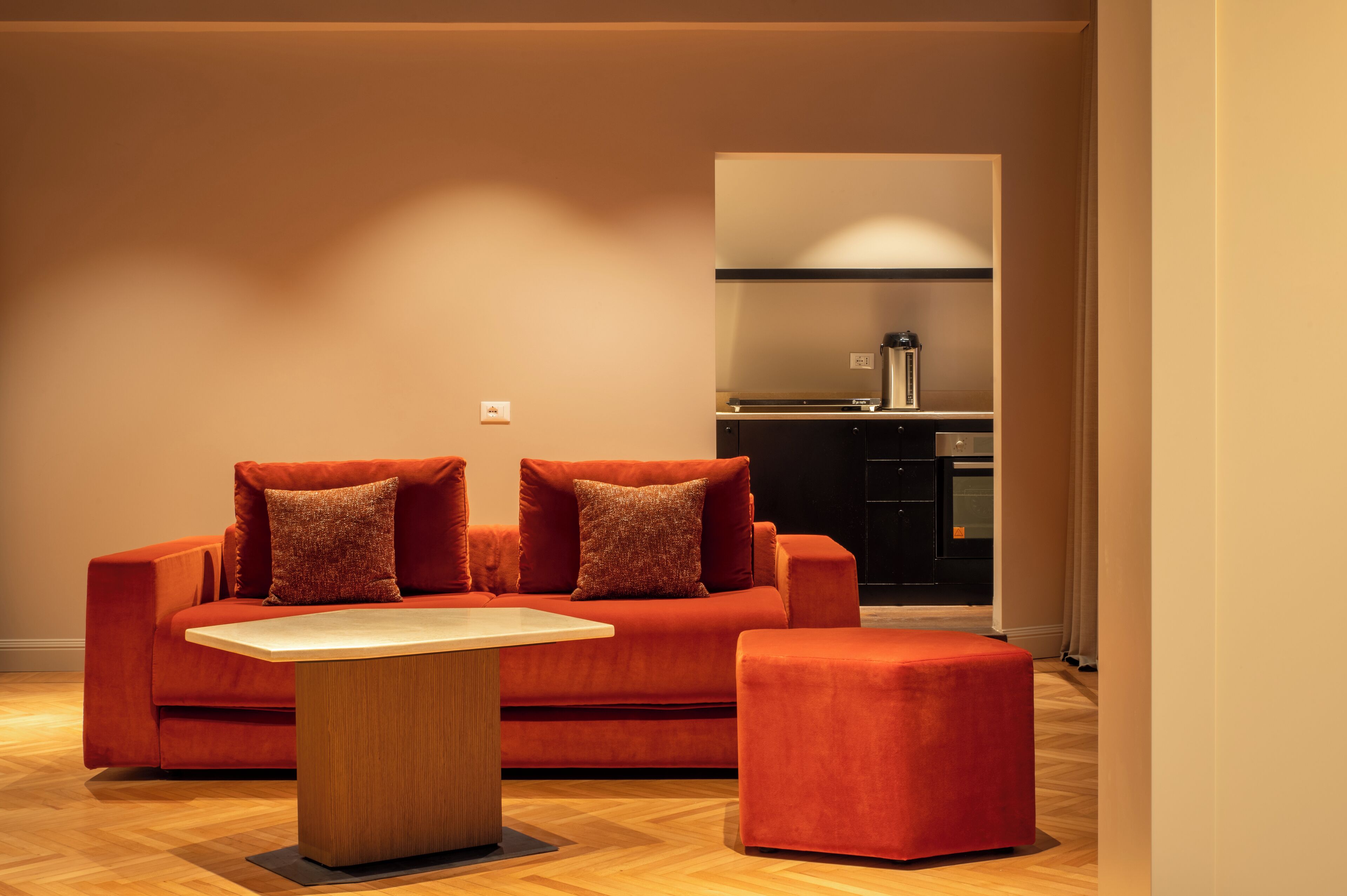 A modern living room with a red sofa set, a wooden coffee table, and a kitchen area in the background.