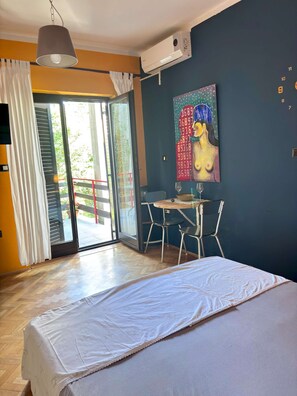 A bedroom with a bed, a table with chairs, a painting, and a sliding glass door leading to an outdoor area.
