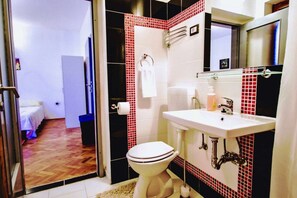 Um banheiro com vaso sanitário branco, pia com espelho em cima e paredes com azulejos vermelhos.