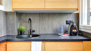 Una cocina moderna con un lavamanos negro, armarios de madera, encimera negra, una pequeña planta en maceta, una botella de agua y un tostador.