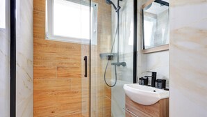 Un baño moderno con cabina de ducha de vidrio, lavamanos blanco y muebles de madera.