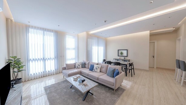 A modern living room with a sectional sofa, a coffee table, and a dining area with a table and chairs. - Mabaat - Al Qirawan - 557 (Riyadh)