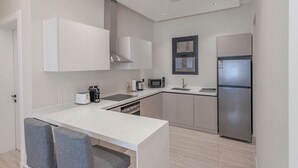 A modern kitchen with white cabinets, a stainless steel refrigerator, a microwave, and a coffee maker. - Mabaat - Al Qirawan - 557 (Riyadh)
