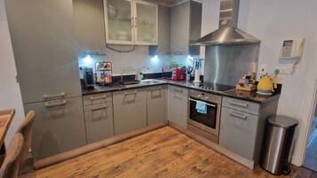 A modern kitchen with grey cabinets, a stainless steel range hood, a built-in oven, and a sink.