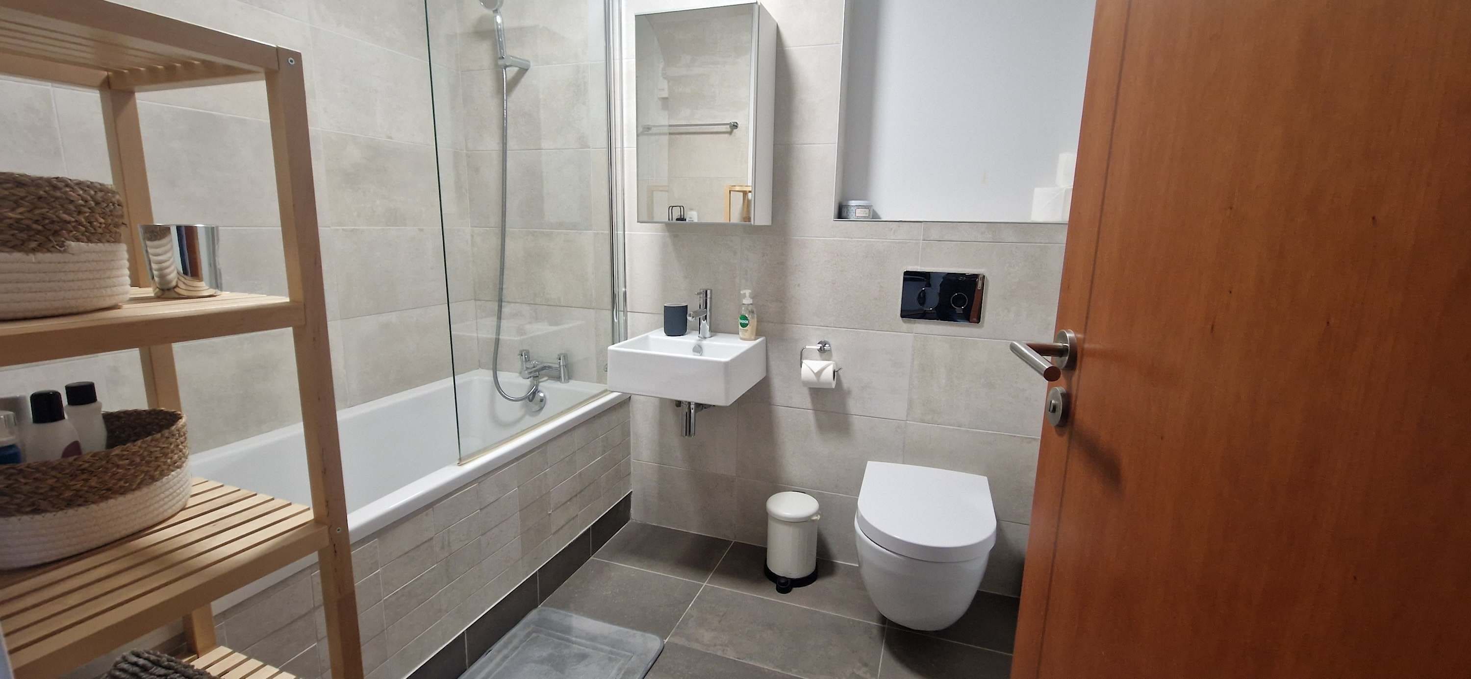 A modern bathroom with a glass shower enclosure, a white sink, a toilet, and a wooden shelf with towels.