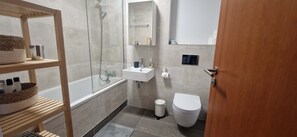 A modern bathroom with a glass shower enclosure, a white sink, a toilet, and a wooden shelf with towels.