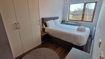 A bedroom with a bed, bedside table, lamp, window, and wardrobe.