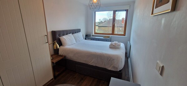 A bedroom with a bed, bedside table, lamp, window, and a view of the outside.