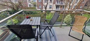 A balcony with a table, chairs, and a small garden area.