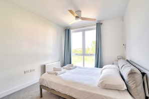 A bedroom with a bed, a ceiling fan, a window with curtains, and a radiator.