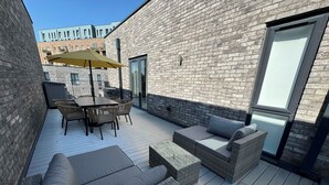 Un patio al aire libre con una mesa, sillas, un sofá y un amplio paraguas.