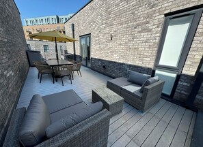 Una terrazza esterna con tavolo e sedie, un divano e un ombrellone.
