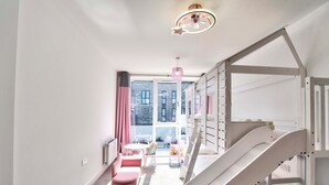 Una habitación infantil con una cama litera, una mesita y una ventana con cortinas.