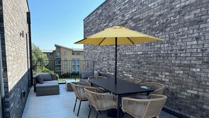 Un patio al aire libre con una mesa, sillas, un paraguas amarillo y un muro de ladrillo.