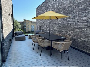 Una terrazza esterna con tavolo e sedie, un ombrello giallo e un muro in mattoni.
