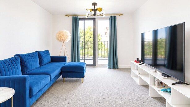 Una sala moderna con un sofá azul, un televisor de pantalla plana grande y una lámpara de pie.