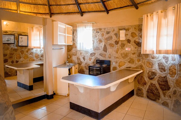 A kitchen with a stone wall backsplash, a central island, and a thatched ceiling. - Thakgalo Honeymoon Suite - 2211 (Figtree)