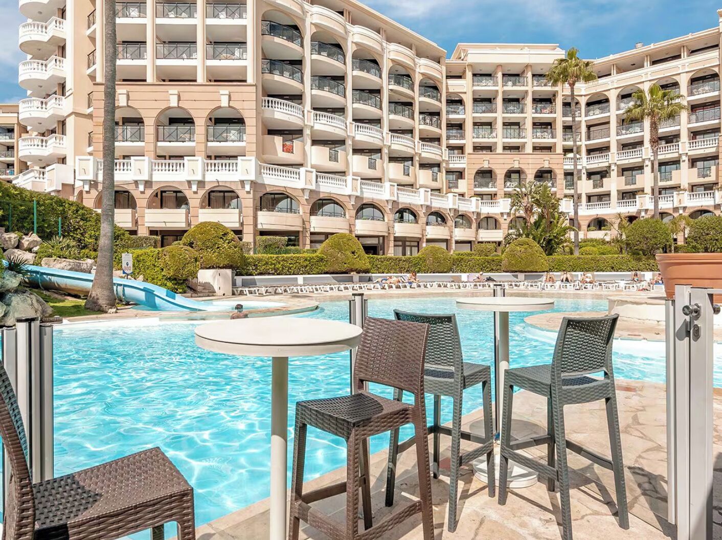 Zona de piscina en un resort, con varias sillas de descanso y un edificio grande con balcones al fondo.