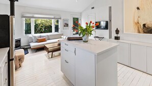 A modern kitchen with white cabinetry, a central island, and a large window providing natural light. - Charming 2-bedroom cottage in Sag Harbor with AC, WiFi (Sag Harbor)
