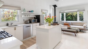 A modern kitchen with white cabinetry, a central island, and a dining area with a sofa and table. - Charming 2-bedroom cottage in Sag Harbor with AC, WiFi (Sag Harbor)