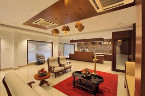 A hotel lobby with a reception desk, two armchairs, a sofa, a coffee table, and a red carpet. - Hotel Indraprastha Kozhencherry (Kozhenchery)
