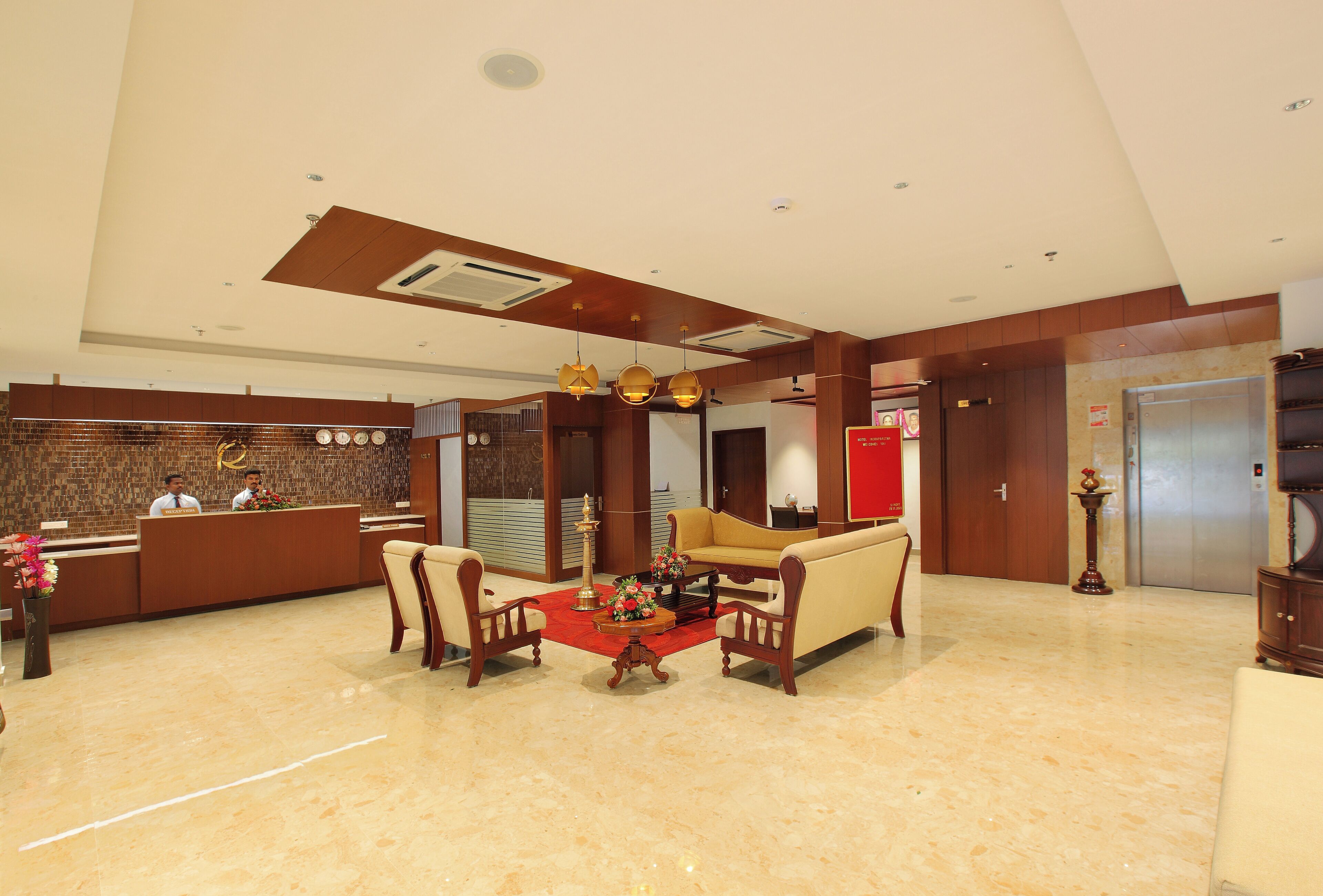 A hotel lobby with a reception desk, a sofa set, a coffee table, and a red carpet.