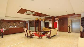 A hotel lobby with a reception desk, a sofa set, a coffee table, and a red carpet.