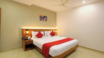 Una habitación de hotel con una cama grande, una mesita de noche con una lámpara, un ventilador de techo y un cuadro en la pared.