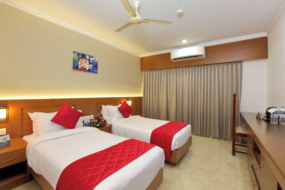 Habitación de hotel con dos camas, un escritorio, un ventilador de techo, un equipo de aire acondicionado y un cuadro en la pared.