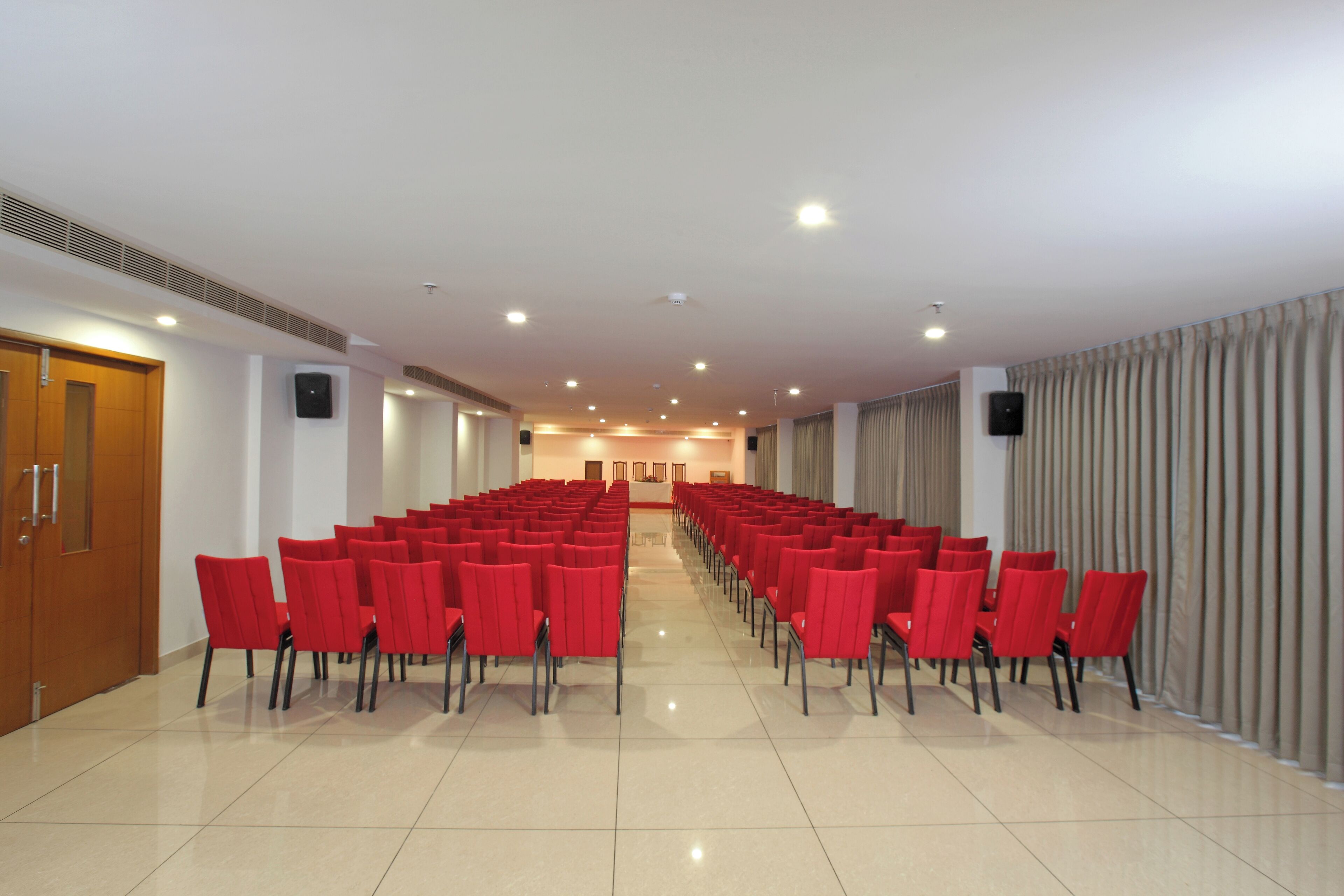 A conference room with rows of red chairs, a wooden door, and a beige tiled floor.