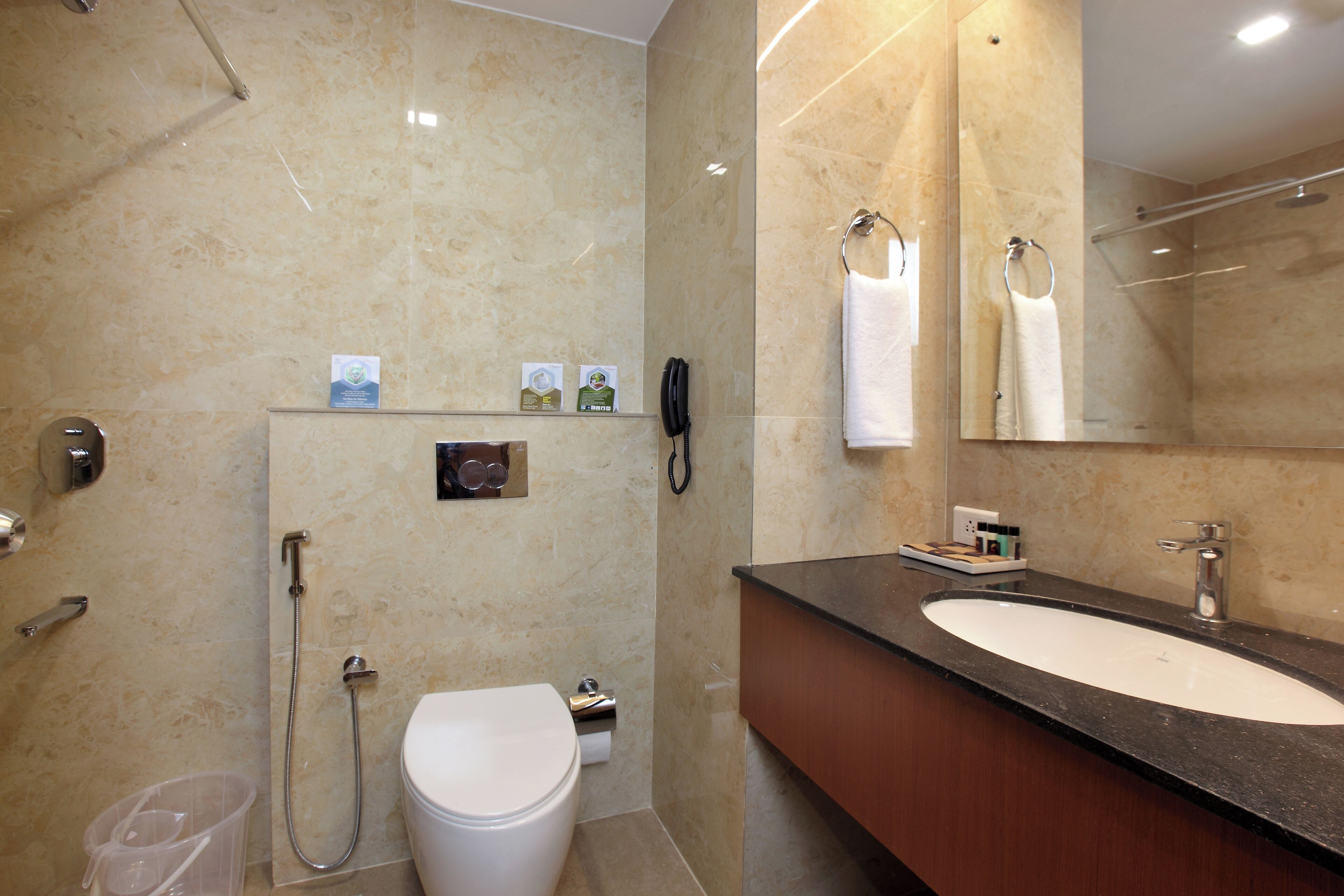 A modern bathroom with a marble wall, a white toilet, a sink with a mirror, and a shower area.