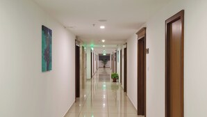 Un pasillo largo y bien iluminado con puertas a ambos lados, una planta en maceta en el centro y una lámpara en el techo.