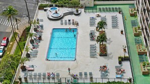 A rooftop pool with multiple swimming areas, sun loungers, and a hot tub.