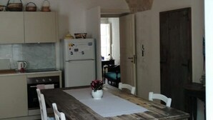 A compact kitchen with a wooden table, white chairs, and a refrigerator. - Le Volte di San Leonardo (Lecce)