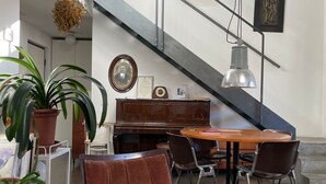 Uma sala de estar moderna com uma poltrona de couro marrom, uma mesa de jantar de madeira e um piano. Há plantas em vasos e uma escada com corrimão de metal.