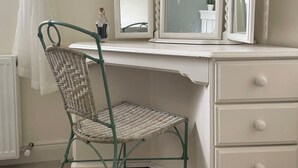 Una habitació amb un tocador blanc, una cadira de vimet i un mirall amb una pintura de bicicleta.