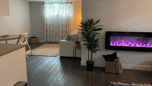 Un salon moderne avec un téléviseur à écran plat fixé au mur, une plante en pot, un canapé et un coin repas comprenant une table et des chaises.