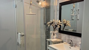 Une salle de bain moderne avec une douche à parois de verre, un meuble-lavabo blanc avec un miroir et un tapis de couleur turquoise.